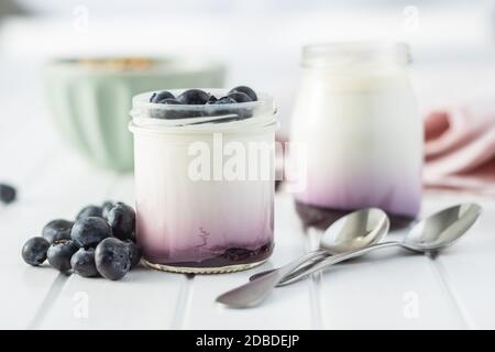 Yogurt bianco fruttato in vaso e mirtilli su tavolo bianco. Foto Stock