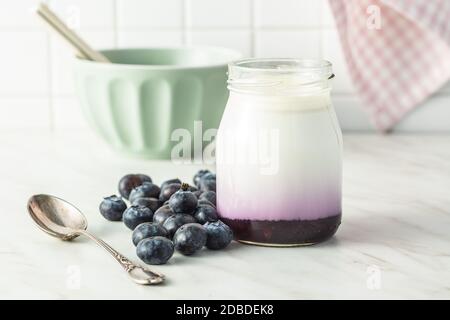 Yogurt bianco fruttato in vaso e mirtilli su tavolo bianco. Foto Stock