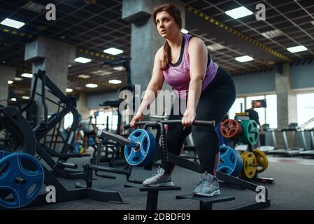 Donna in sovrappeso che fa esercizio con bar in palestra, allenamento attivo. La persona femminile obesa lotta con il peso in eccesso, allenamento aerobico contro l'obesità, s. Foto Stock