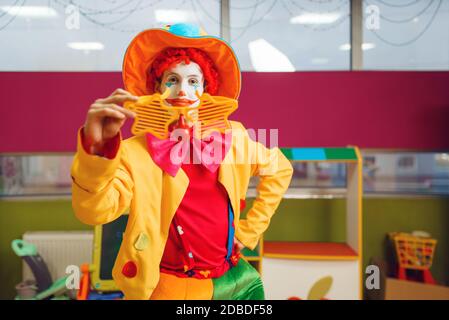 Un clown divertente in occhiali da stella si pone nell'area dei bambini. Festa di compleanno in sala giochi, baby Holiday in parco giochi. Felicità infantile, bambino Foto Stock