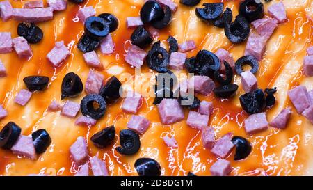 Ingredienti su pizza cruda close-up.Ulivi e salsiccia affettata si trovano su un impasto di pizza unto con pasta di pomodoro. Cucina della pizza a casa. Foto Stock