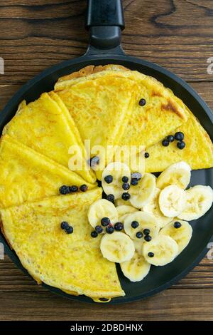 Gustosi pancake con banane e mirtilli su padella nera. Vista in primo piano. Frittelle fatte in casa. Pancakes colazione cibo. Foto Stock
