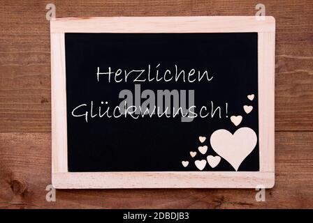 Balckboard con testo tedesco Herzlichen Glueckwunsch significa Complimenti. Decorazione rustica cuore di legno. Marrone legno sfondo Foto Stock