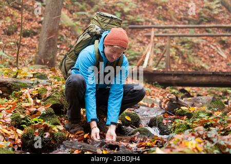 Backpacker scoping acqua da un torrente di montagna in autunno - mettere a fuoco il viso Foto Stock