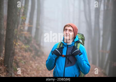 Giovane uomo trekking con zaino in una foresta in inverno - mettere a fuoco il viso Foto Stock