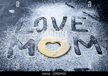 Concetto di Mather Day. Parola AMORE MOM fare dalla farina e l'impasto su sfondo scuro. Viste dall'alto, primo piano. Foto Stock