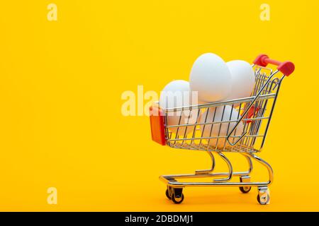 Le uova di pollo bianche sono nel carrello della drogheria, sfondo arancione brillante Foto Stock