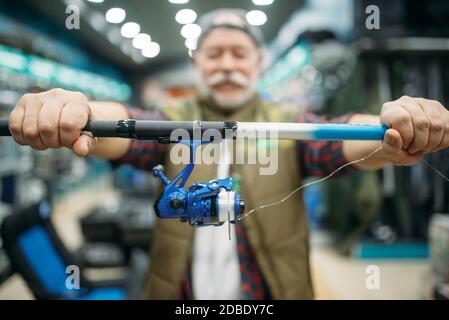 Il pescatore maschile mostra canna con bobina in negozio di pesca. Attrezzature e strumenti per la cattura e la caccia del pesce, scelta di accessori in vetrina in negozio, spinning a. Foto Stock