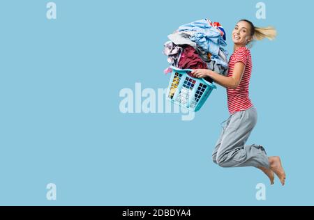 Felice donna allegra facendo lavanderia e saltando, sta tenendo un cesto di bucato riempito di vestiti Foto Stock