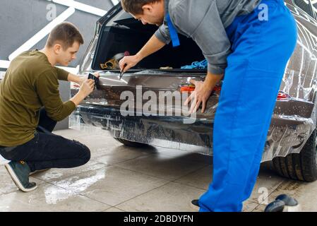 Gli specialisti applicano la pellicola di protezione dell'auto sul paraurti posteriore. Installazione di un rivestimento che protegge la vernice dell'automobile dai graffi. Veicolo nuovo in g Foto Stock