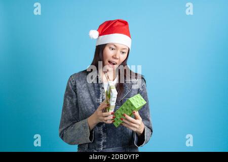 Sorpresa Asiatica giovane donna nel cappello di Babbo Natale apre la scatola regalo di nuovo anno, su sfondo blu Foto Stock