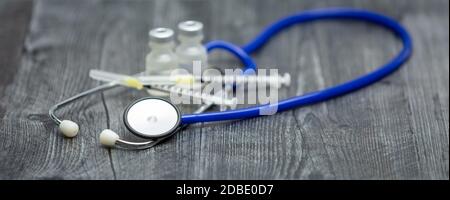 Uno stetoscopio medico blu, siringhe e flaconcini si trovano su una superficie di legno. Foto Stock
