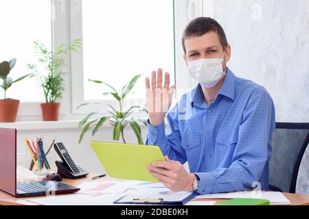 Ritratto di un lavoratore in ufficio in una maschera medica che lavora da remoto Foto Stock