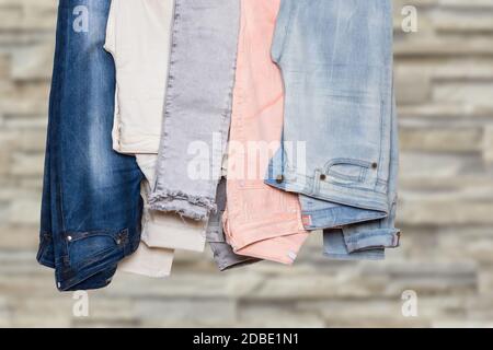 Primo piano della collezione di cinque pantaloni denim femmina vari o pantaloni colorati su una ringhiera contro la parete di cemento grigio chiaro sfocato. Jeans moda Foto Stock