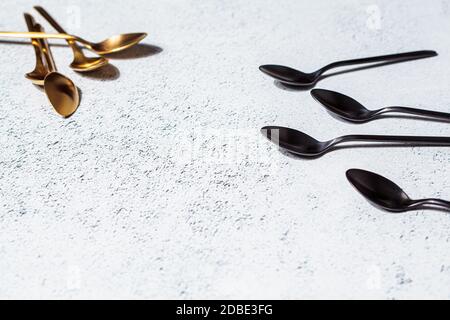 Cucchiai da dessert dorati e neri vuoti su sfondo grigio, spazio copia. Mangiare cibo concetto. Posate vuote sullo sfondo. Foto Stock