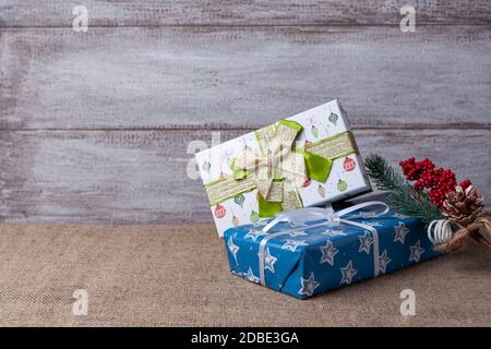 Cartolina fatta di scatole regalo blu e verde, ramo dell'albero di Natale con decorazioni su sfondo di legno e burlap Foto Stock