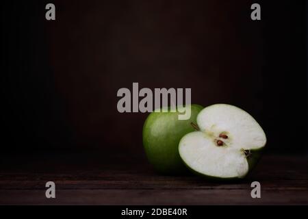 Due mele granny smith, una intera e una tagliata a metà. Due mele granny smith con vecchia caraffa in ceramica. Scatto a livello degli occhi con un tocco rustico scuro e co Foto Stock