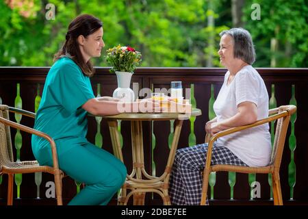 Sorridente giovane accompagnatore che serve la colazione per una donna anziana felice a casa di cura Foto Stock