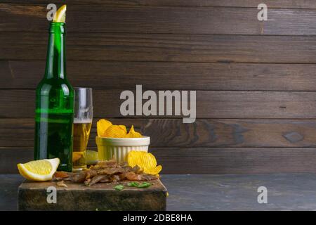 Bastoncini di pesce carpe secchi con birra, limoni e patatine su tavola di legno scuro. Spuntino a base di pesce con birra. Vista frontale con spazio libero. Foto Stock