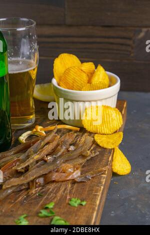 Bastoncini di pesce carpe secchi con birra, limoni e patatine su tavola di legno scuro. Spuntino a base di pesce con birra. Primo piano. Foto Stock