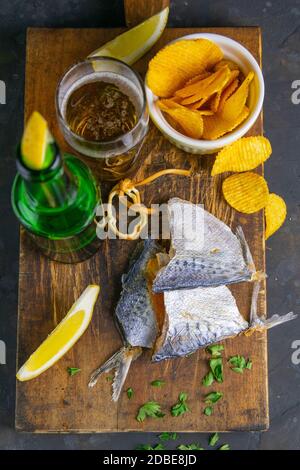 Orata secca in forma di farfalla con birra, limoni e patatine su tavola di legno scuro. Spuntino a base di pesce con birra. Primo piano. Foto Stock