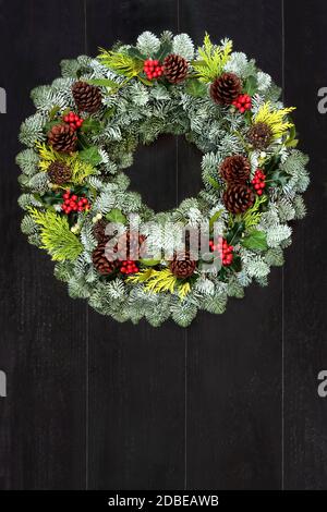 Inverno naturale e solstice verde corona con abete rosso, agrifoglio, cedro e mistletoe su rustico sfondo di legno scuro. Simbolo tradizionale per Natale. Foto Stock