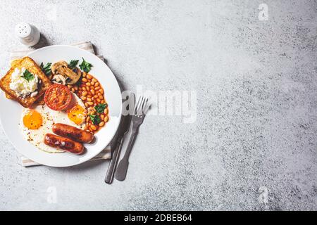 Colazione inglese con salsicce, fagioli, uova fritte, toast, funghi e pomodori in un piatto bianco. Concetto di colazione inglese. Foto Stock