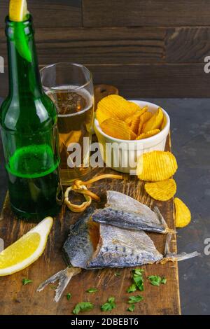 Orata secca in forma di farfalla con birra, limoni e patatine su tavola di legno scuro. Spuntino a base di pesce con birra. Primo piano. Foto Stock