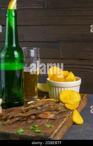 Bastoncini di pesce carpe secchi con birra, limoni e patatine su tavola di legno scuro. Spuntino a base di pesce con birra. Primo piano. Foto Stock