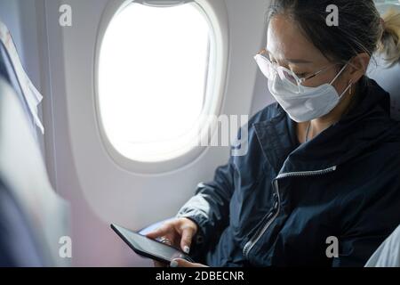 donna asiatica passeggero femminile seduto in cabina di lettura aereo ebook con lettore di e-reader Foto Stock