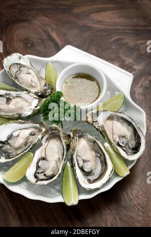 Sei ostriche fresche con spicchi di lime e salsa di vinaigrette agli agrumi Foto Stock