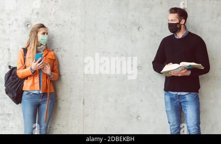 Due studenti in piedi a distanza sociale indossando maschera di viso guardando l'uno all'altro Foto Stock