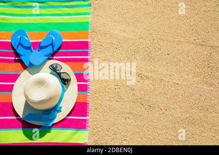 Telo da spiaggia con cappello, occhiali da sole e infradito fotografato dall'alto sulla spiaggia di sabbia, caldi accessori estivi, destinazione di vacanza, soleggiata spiaggia tropicale sfondo Foto Stock