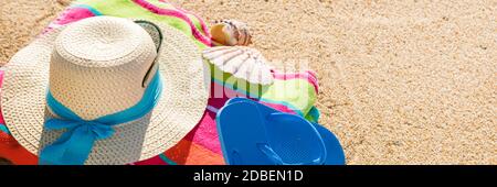 Telo da spiaggia con cappello, occhiali da sole e infradito fotografato dall'alto sulla spiaggia di sabbia, caldi accessori estivi, destinazione di vacanza, soleggiata spiaggia tropicale sfondo Foto Stock