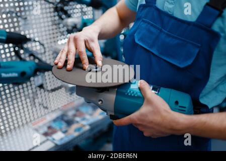 Uomo in uniforme scelta del disco bordato per smerigliatrice angolare in magazzino utensili. Scelta di attrezzature professionali nel negozio di ferramenta, supermercato di strumenti Foto Stock
