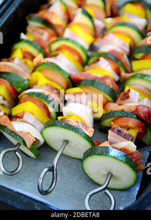 Teglia piena di spiedini metallici con carne di maiale cruda e verdure pronte per la cottura. Foto Stock