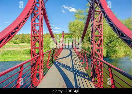 Via ferro rosso sospensione ponte pedonale sul fiume Irpin dal terrapieno al bosco verde. Foto Stock