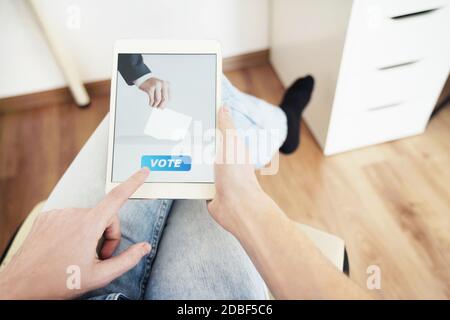 Uomo che voterà online a casa utilizzando il tablet digitale. Foto Stock