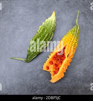 Due meloni amari - con pelle verde increspata e polpa arancione soprammatura, divisi per mostrare i semi rossi - su uno sfondo grigio ardesia Foto Stock