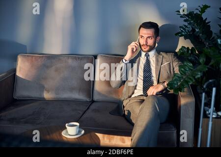 Scontento uomo d'affari su un divano che ascolta notizie al telefono Foto Stock