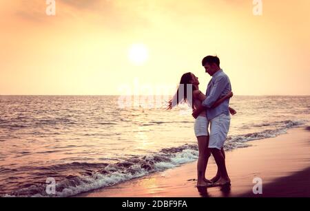Romantica giovane coppia abbraccio sulla spiaggia al tramonto Foto Stock