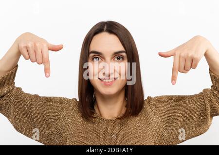 giovane bella ragazza che si mostra in giù in un maglione d'oro sopra una foto promozionale concettuale di sfondo bianco Foto Stock