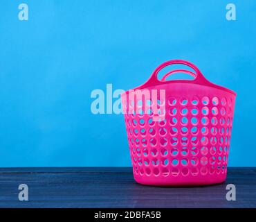 cesto rosa di plastica nel foro per biancheria pulita e sporca, vestiti su sfondo blu, contenitore, spazio per la copia Foto Stock