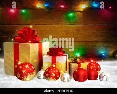 Le sfere di vetro rosso a tema natalizio, le scatole regalo dorate con archi sulla parete di fondo in legno con luci di natale multicolore luminose e spazio libero Foto Stock