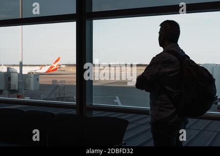 Silhouette di un uomo nella lounge dell'aeroporto mentre aspettate la partenza dell'aereo, guardando l'aereo all'esterno Foto Stock