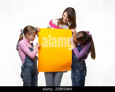 Mamma e due figlie tengono un segno arancione nelle loro mani e lo guardano Foto Stock