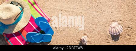 Telo da spiaggia con cappello, occhiali da sole e infradito fotografato dall'alto sulla spiaggia di sabbia, caldi accessori estivi, destinazione di vacanza, soleggiata spiaggia tropicale sfondo Foto Stock