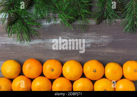 Tangerini con rami di pino e coni su fondo di legno marrone. Cartolina per Natale e Capodanno. Layout orizzontale. Vista dall'alto Foto Stock