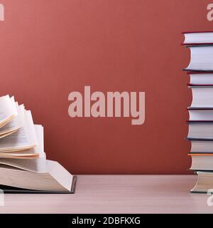 Un libro grande, duro spesso sta sdraiandosi su un tavolo di legno chiaro. Il libro è aperto, accanto a una pila di libri chiusi, e sul retro è uno sfondo marrone Foto Stock