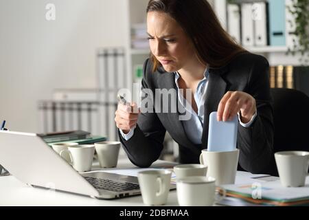Donna esecutiva sovra-lavorata commette errori a causa dell'esaurimento con diverse tazze di caffè sedute di notte in ufficio Foto Stock